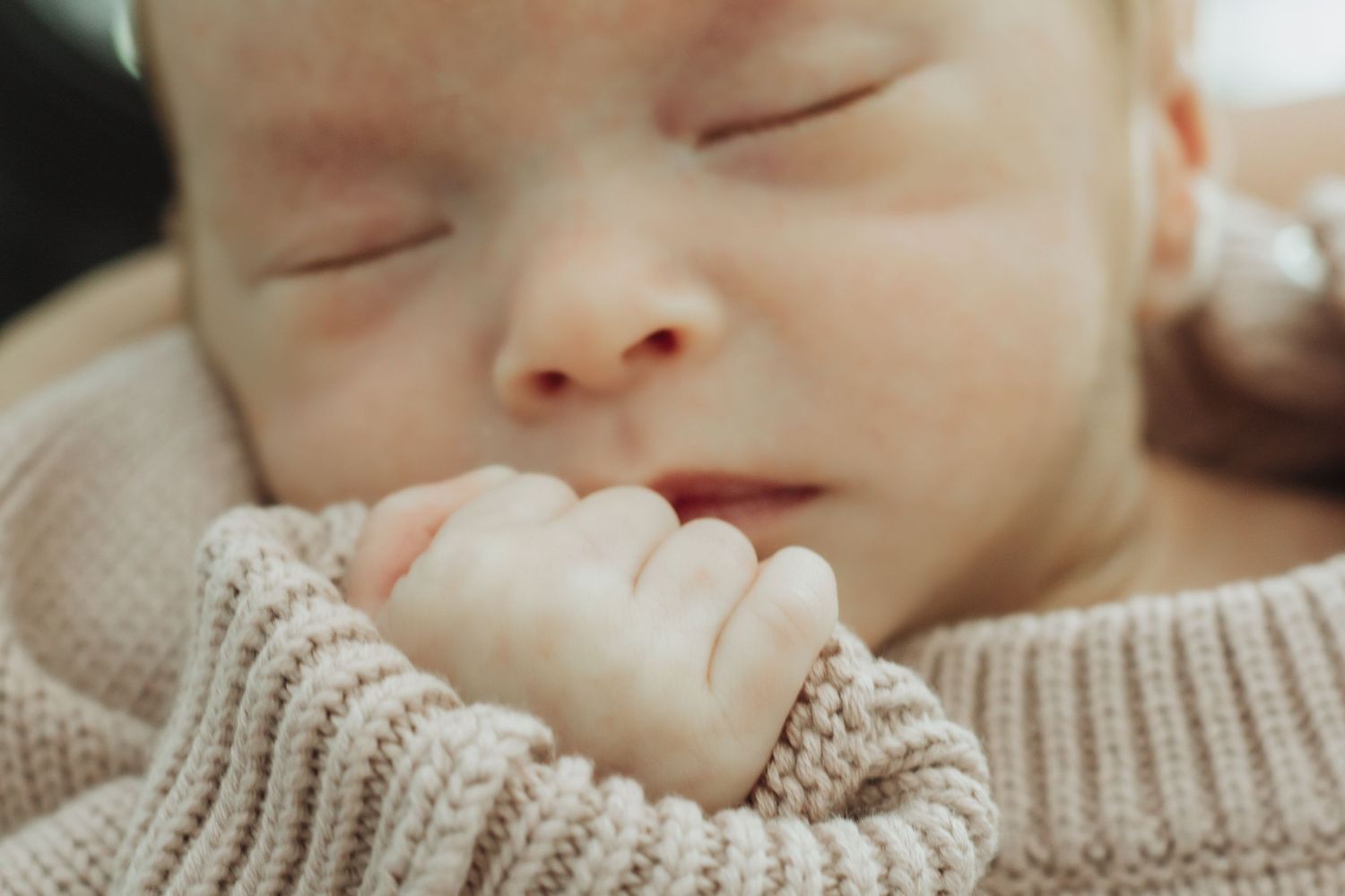 Peaceful sleeping newborn baby in a cozy knit sweater, tiny hand resting near face, close-up portrait photography.