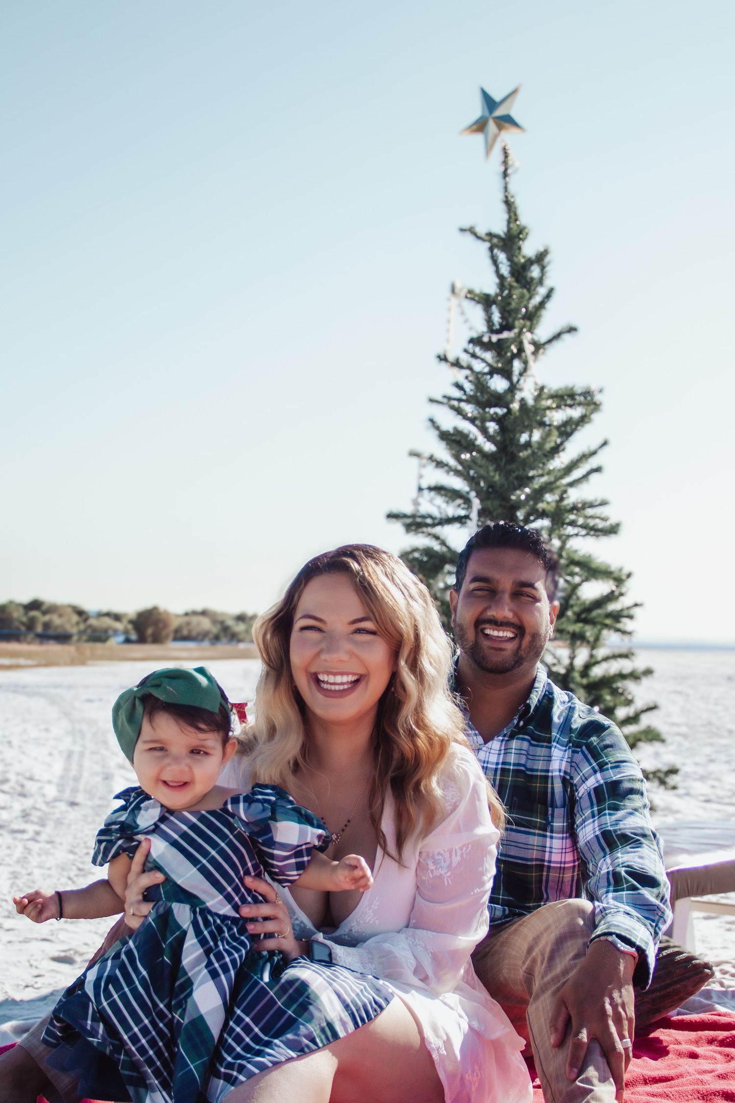 Family enjoying a picnic by the water with evergreen trees in the background on a sunny day.