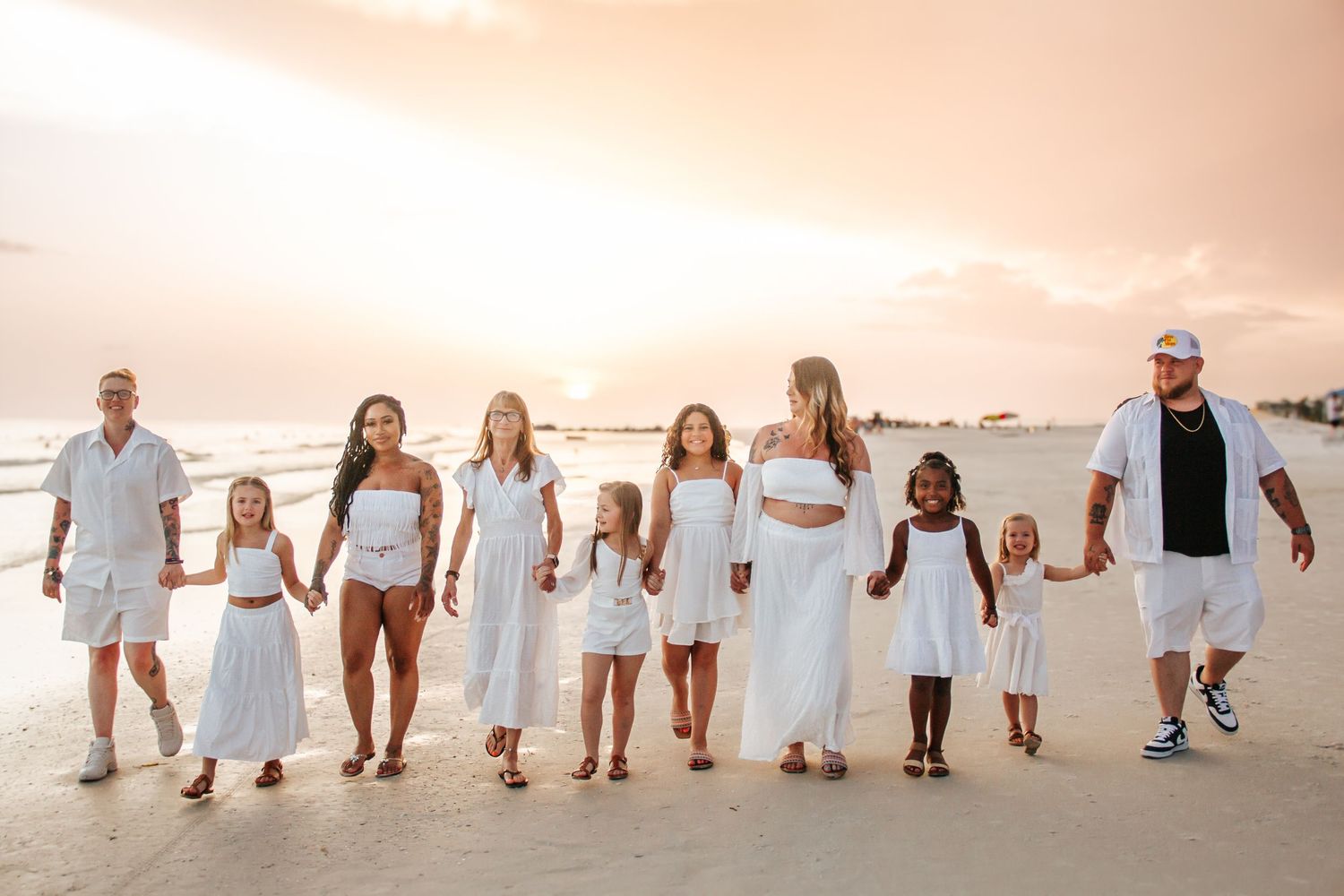 Group walking in line along beach at sunset wearing coordinated white outfits.