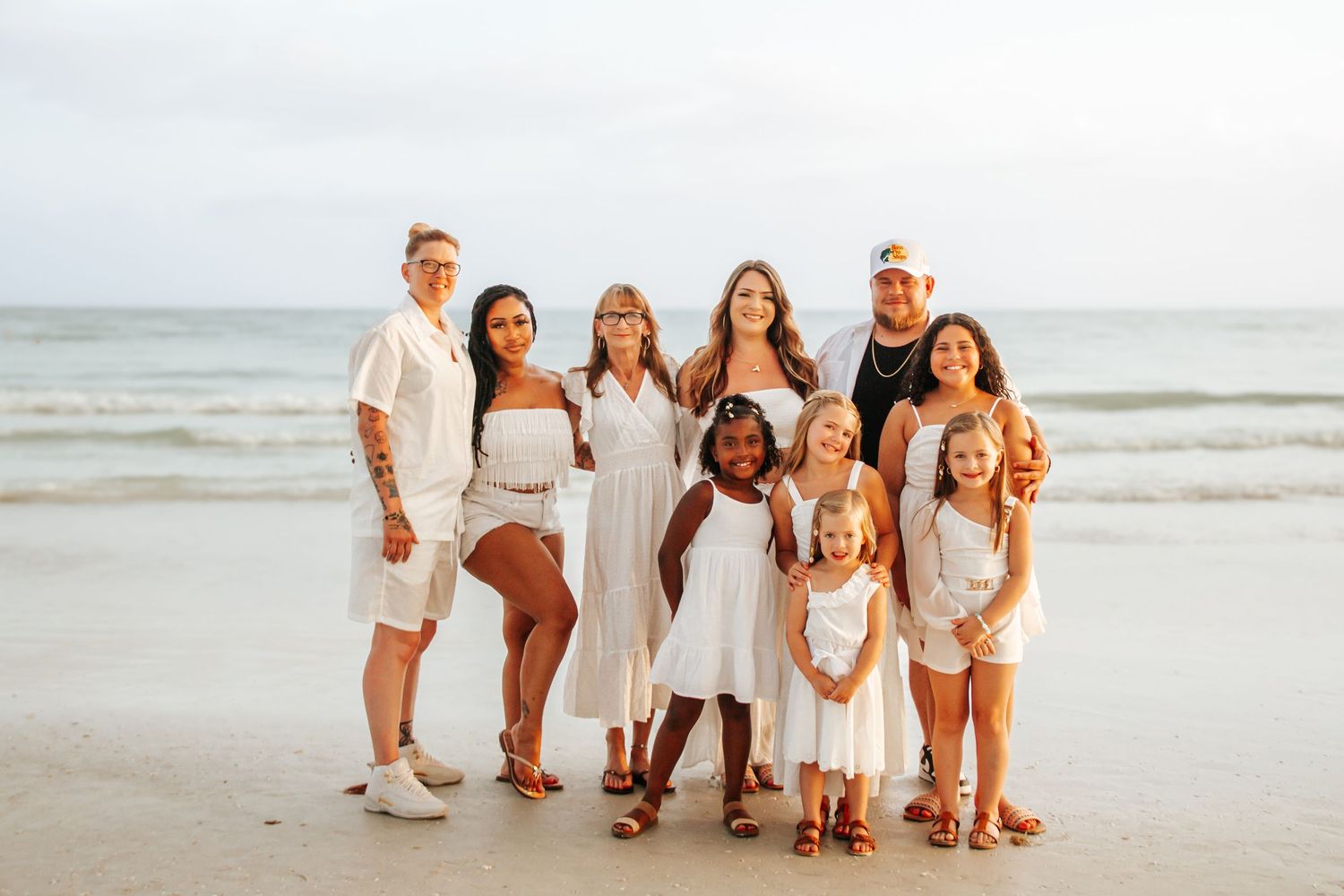 Group portrait on beach with everyone wearing coordinated white and neutral colored outfits.