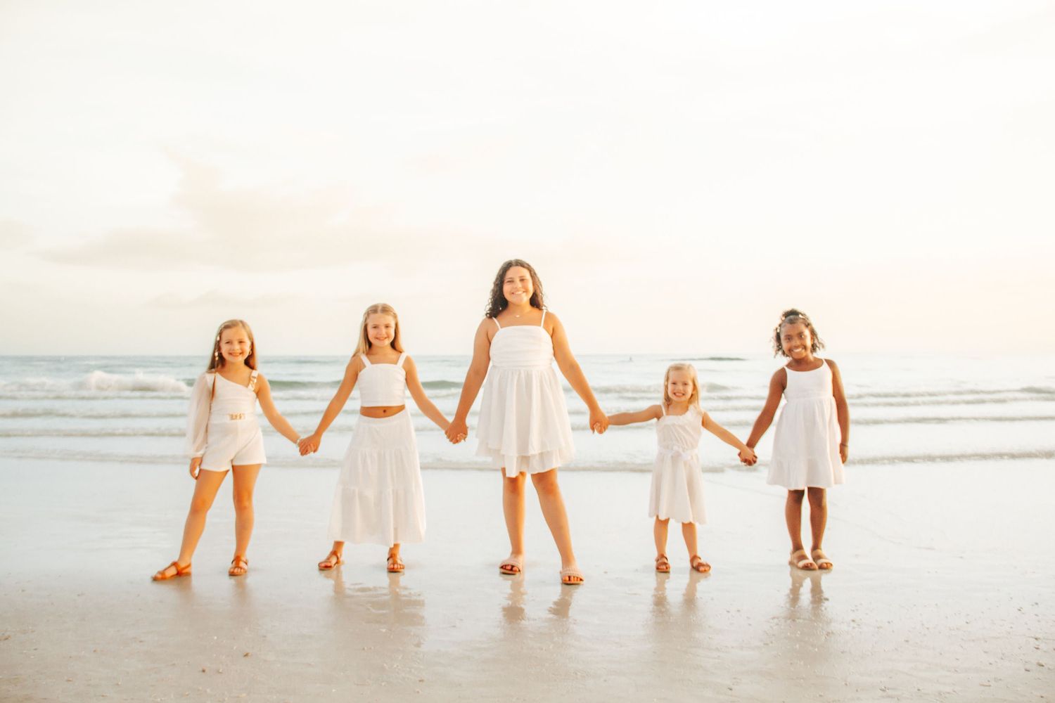 A group of people holding hands while walking in line along a sandy beach at sunset.