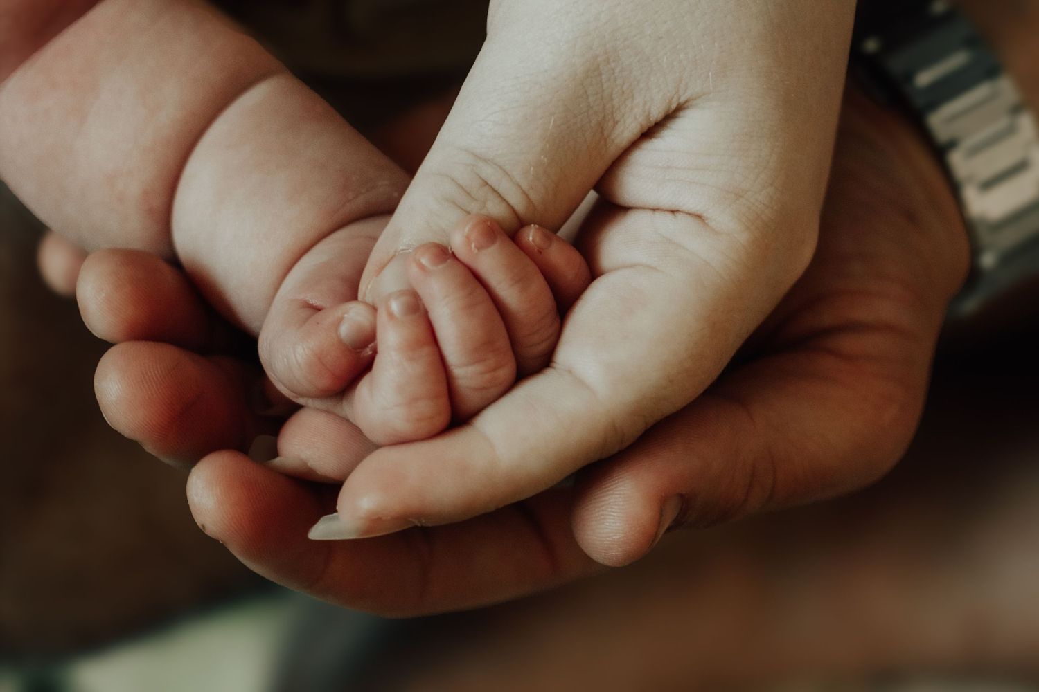 Adult hands gently cradling a newborn baby's tiny fist, symbolizing love, protection, and new parenthood.