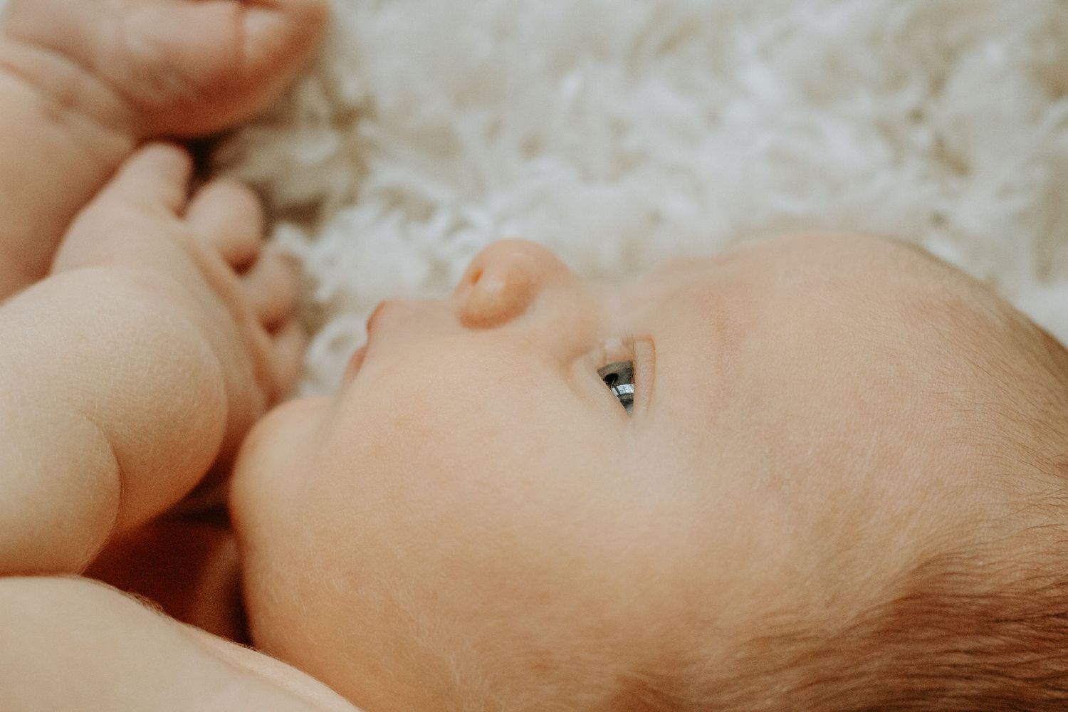Close-up portrait of a peaceful newborn baby lying on a soft white fluffy blanket, with delicate features.