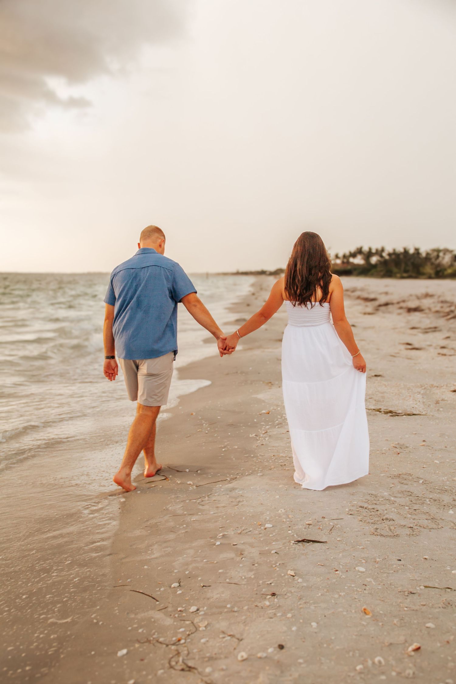 Couple holds hands while walking along a sandy beach at sunset during a romantic coastal stroll.
