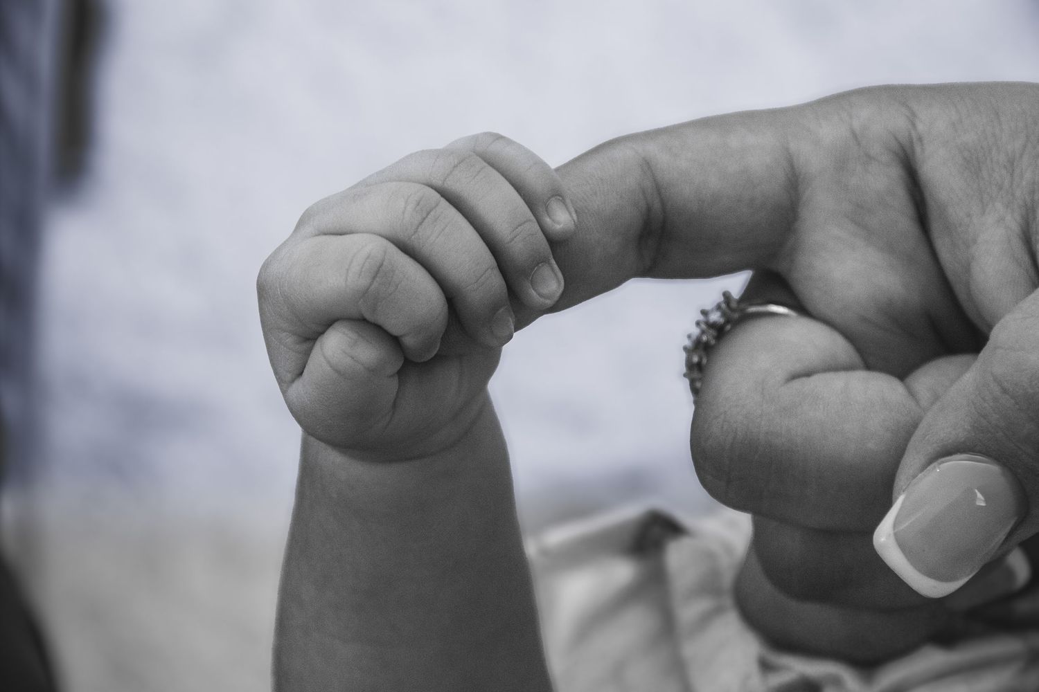 Black and white photo of a newborn baby grasping an adult's finger, symbolizing new life and parental bond.