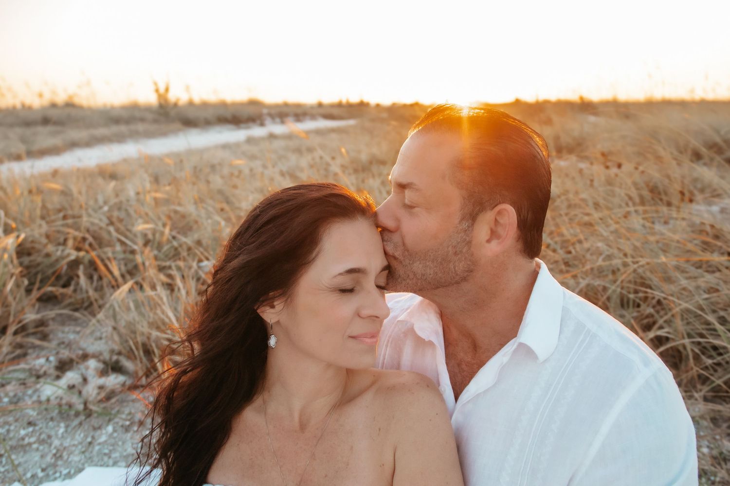 Romantic couple sharing a tender kiss at golden hour on a beach with warm sunset light.