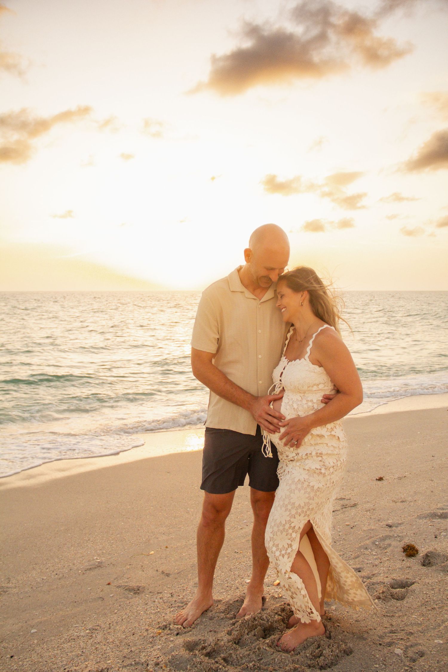 A couple shares a tender moment walking on a tropical beach at sunset.