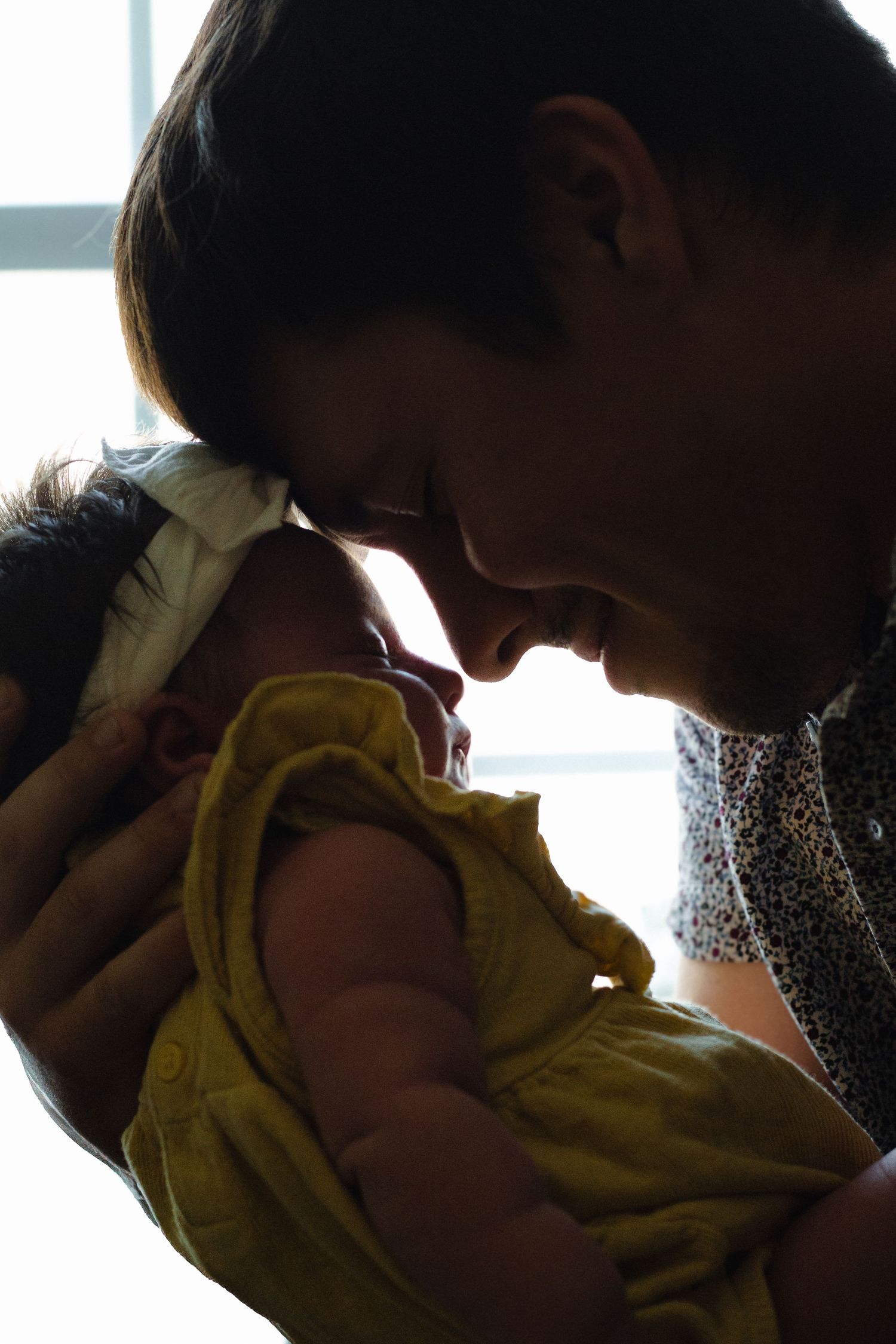 Parent tenderly touching foreheads with newborn baby dressed in yellow outfit in a warm intimate moment.