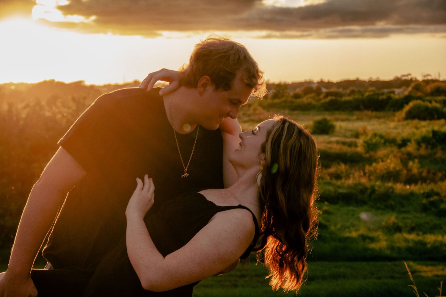 Couple sharing a romantic kiss at golden sunset in a lush green field.