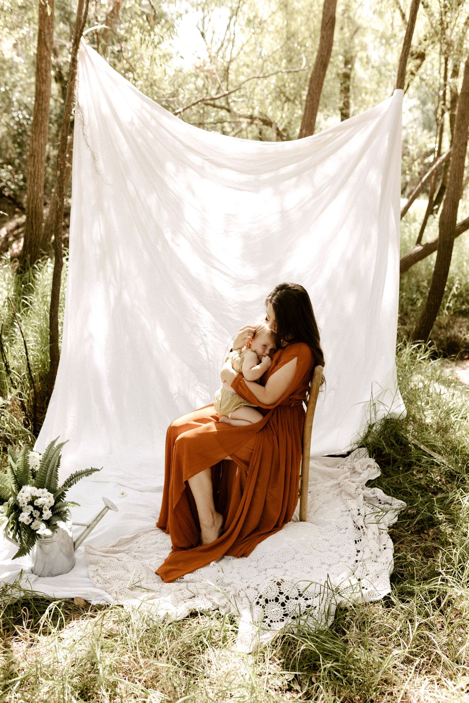 Artistic maternity photoshoot with white backdrop and flowing dress in dreamy forest setting.