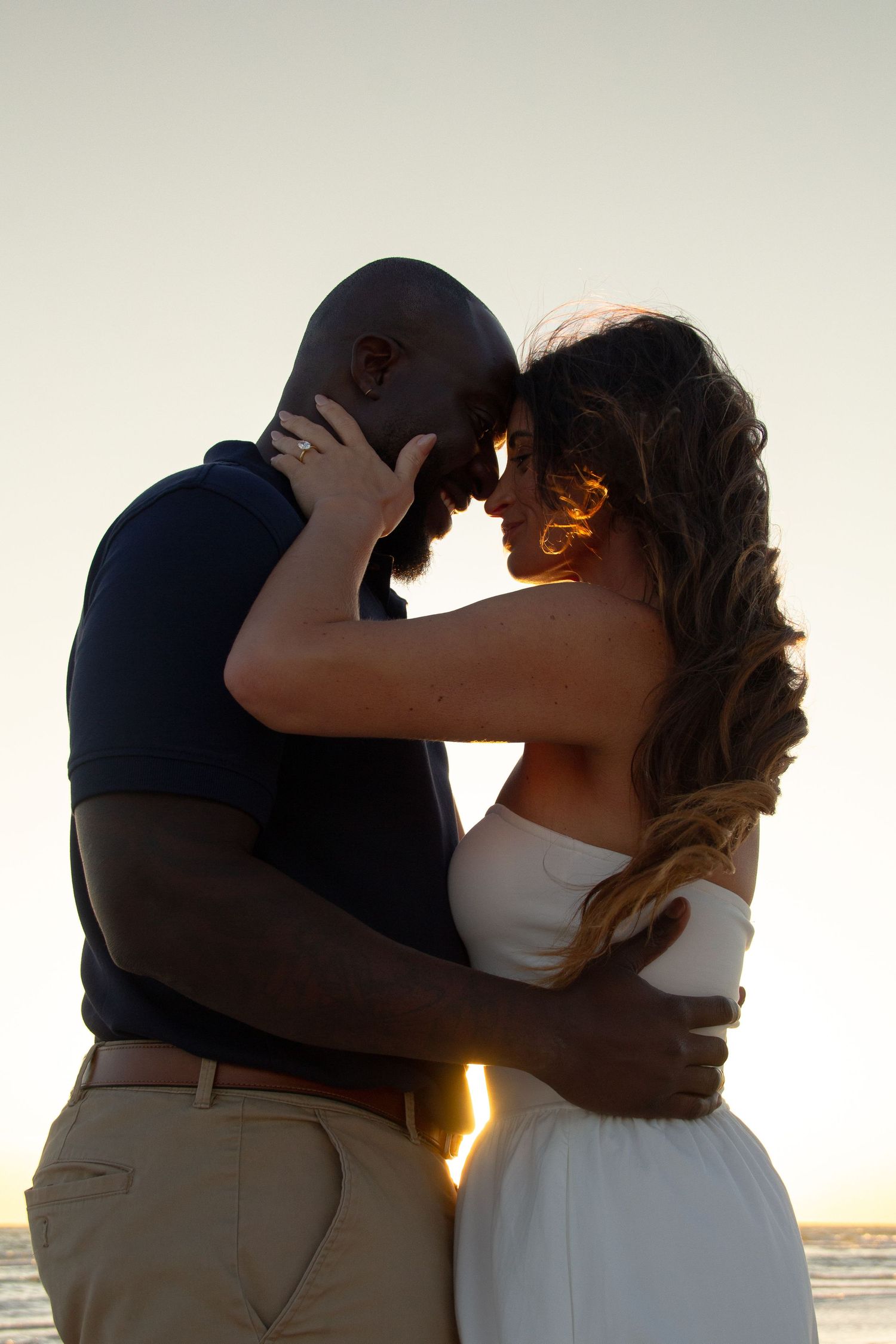 Romantic interracial couple embracing at sunset on the beach, touching foreheads in an intimate moment.