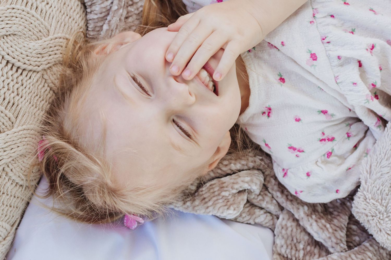 Candid expressions captured while resting on beige knitted blanket with floral print dress.