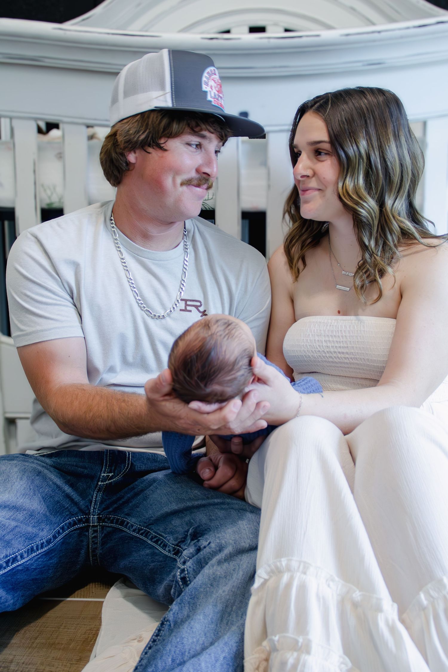 A young couple sitting together, smiling at each other while tenderly holding their newborn baby.