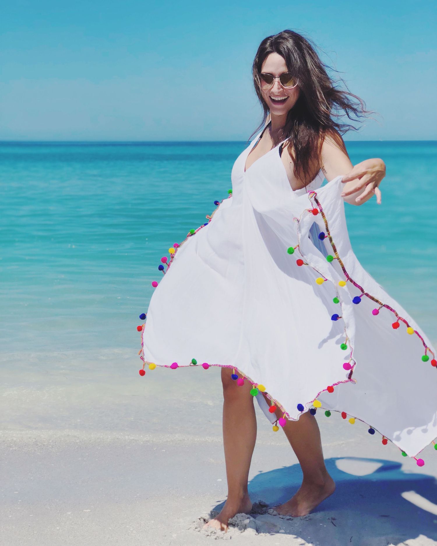 White beach cover-up with colorful pom poms flutters in the wind against turquoise ocean waters.