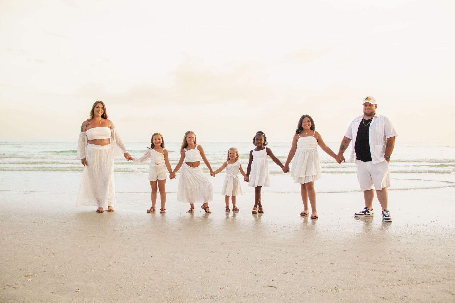 Family members walking together on a sunny beach wearing white outfits at sunset.
