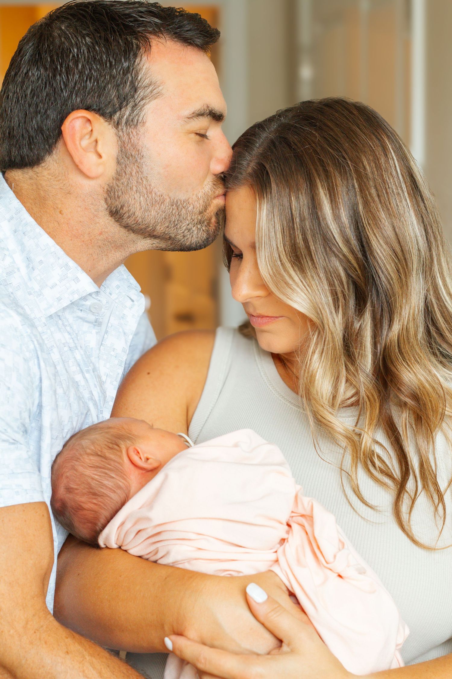 Intimate family moment as parents embrace while holding their newborn baby wrapped in a soft pink blanket.