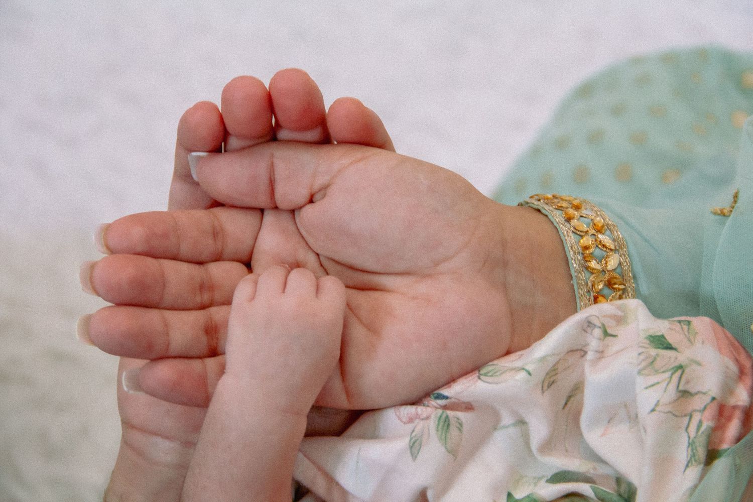 Close-up of a mother's hand gently holding her newborn baby's tiny feet, wearing a gold bracelet.