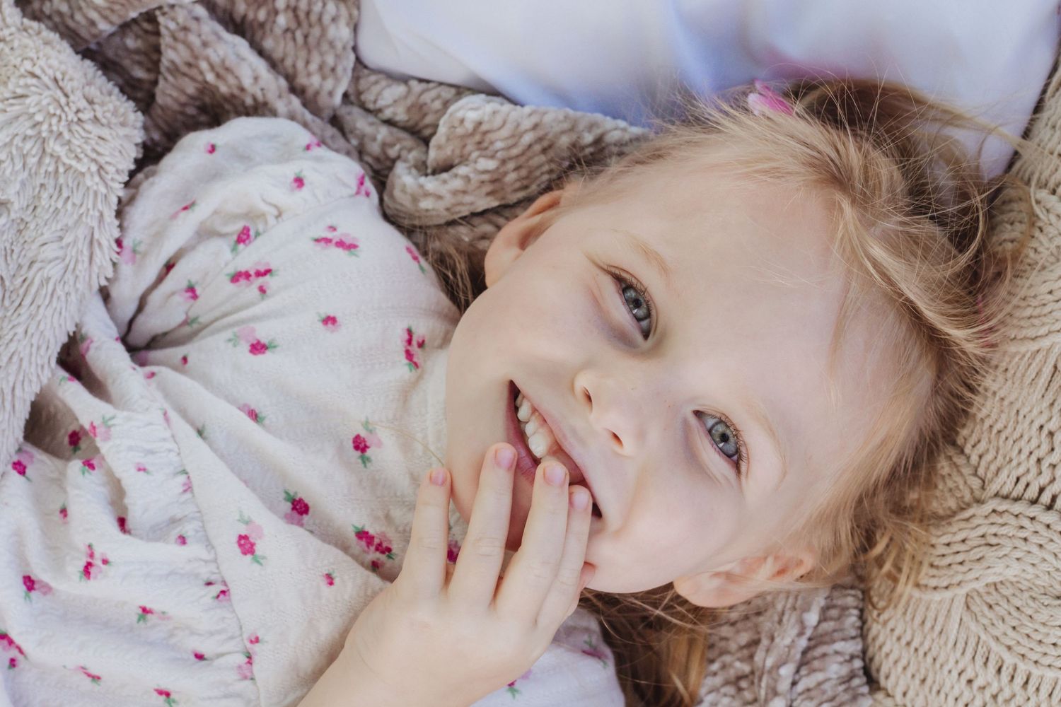 Close up portrait of young person lying on knit blanket with delicate floral print clothing.