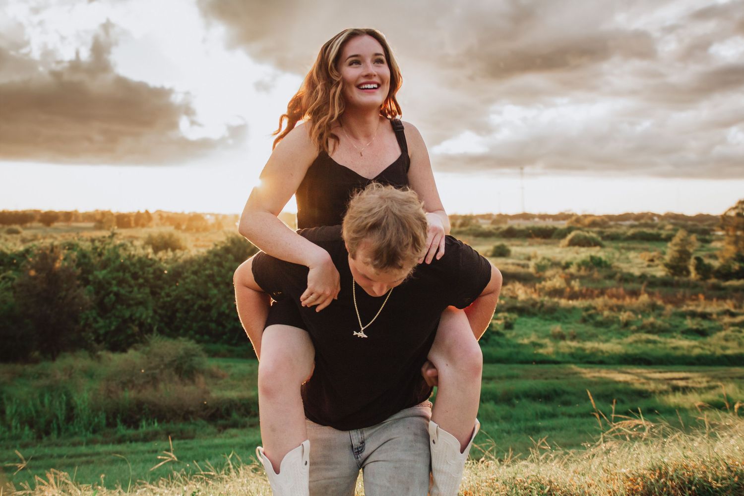 Happy couple at sunset, woman sitting on mans shoulders laughing outdoors.
