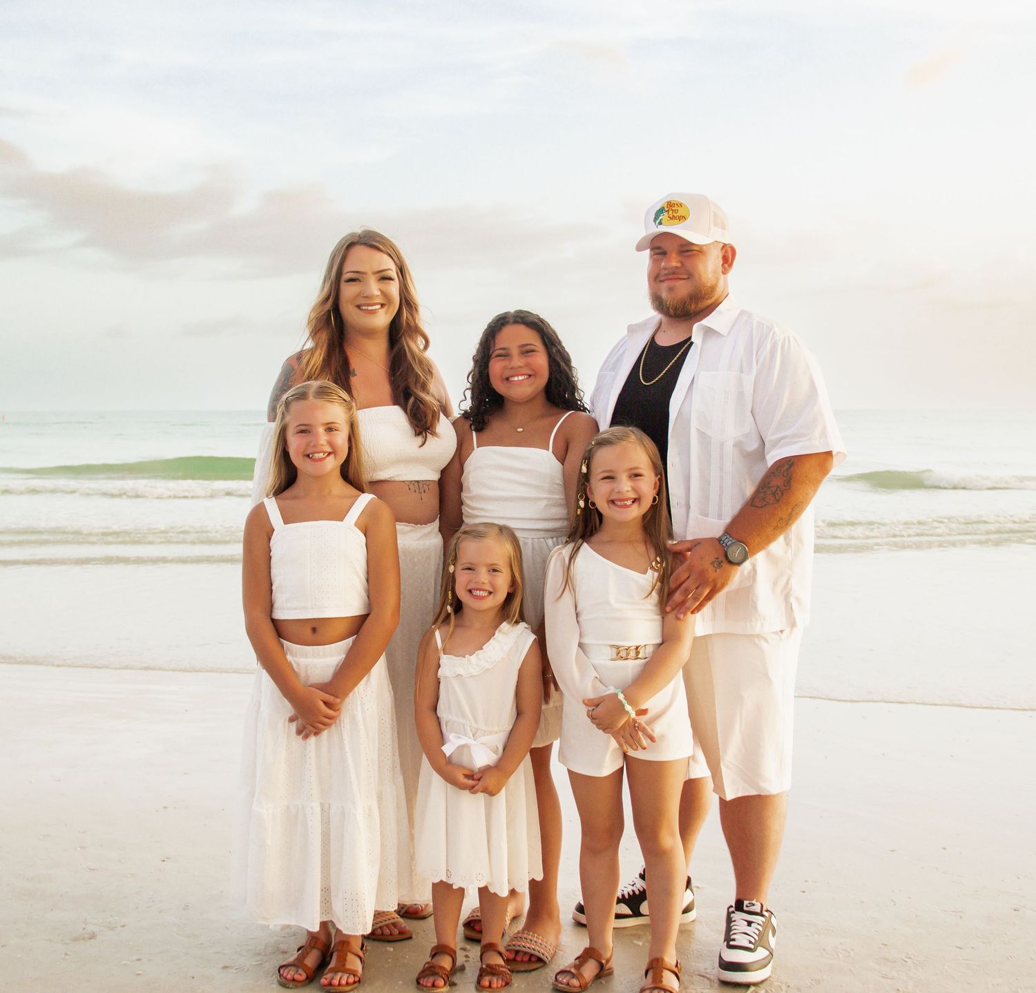 Family group portrait on beach at sunset wearing coordinated white and neutral outfits.