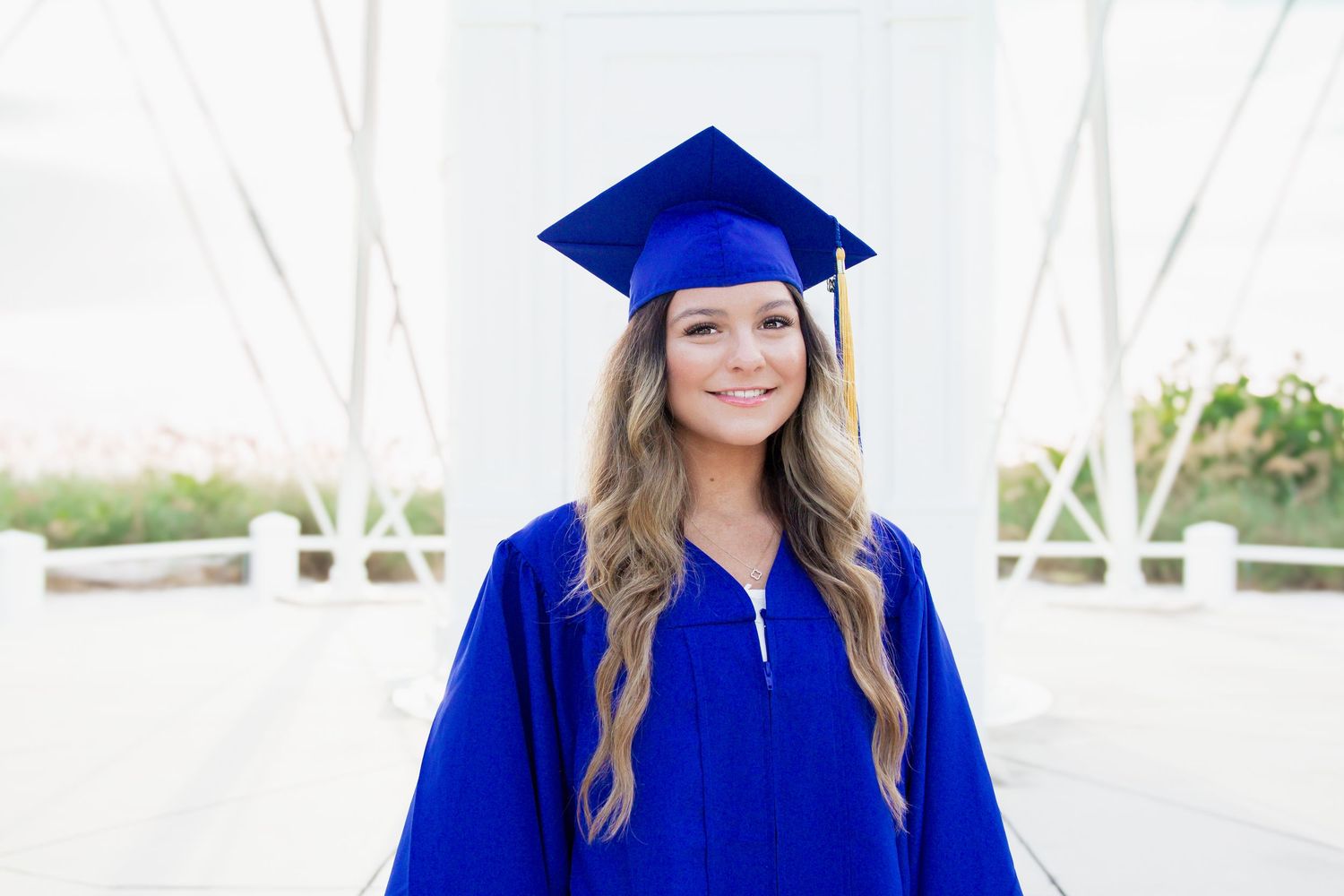 Smiling young woman in blue graduation cap and gown posing outdoors at graduation ceremony.