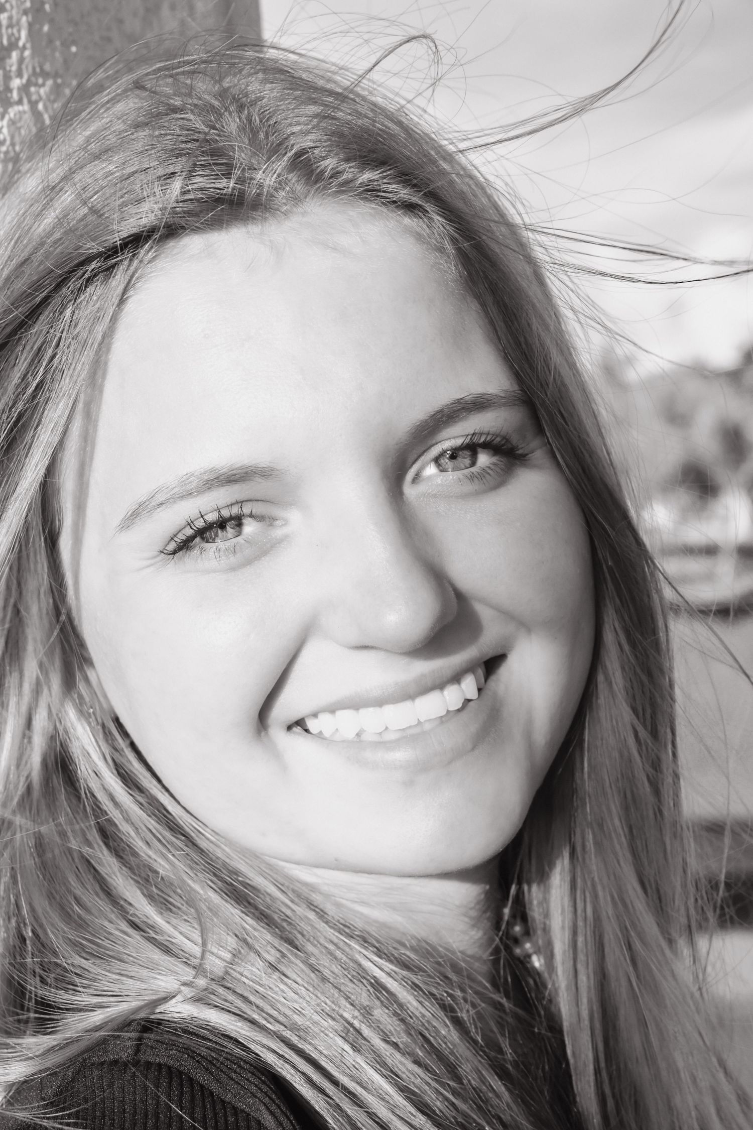 Black and white portrait of a smiling young woman with long hair outdoors.