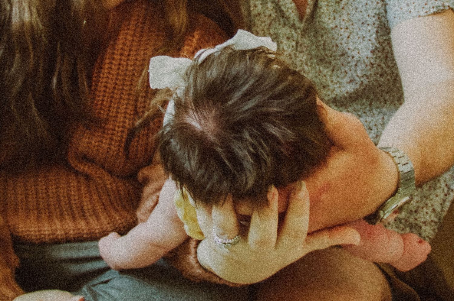 Parents cradling a newborn baby with a white bow in dark hair, captured in warm tones.