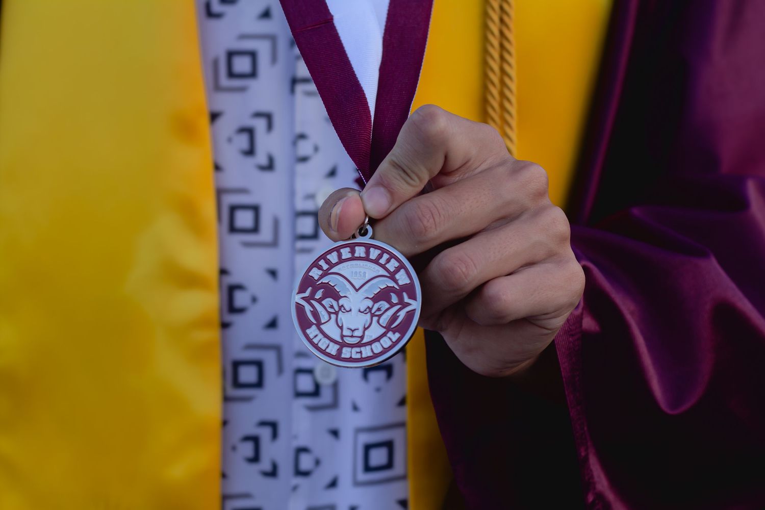 Graduate holding a maroon and silver honor medal with an eagle emblem on a burgundy ribbon at graduation ceremony.