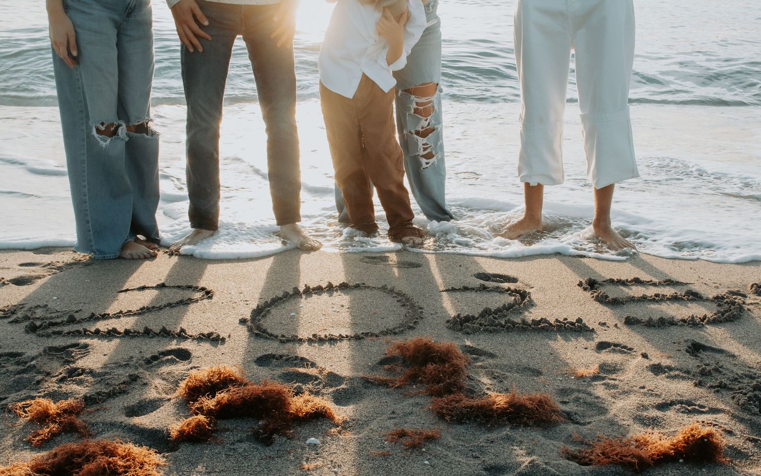 Group of friends standing on sandy beach with numbers written in sand near ocean waves.