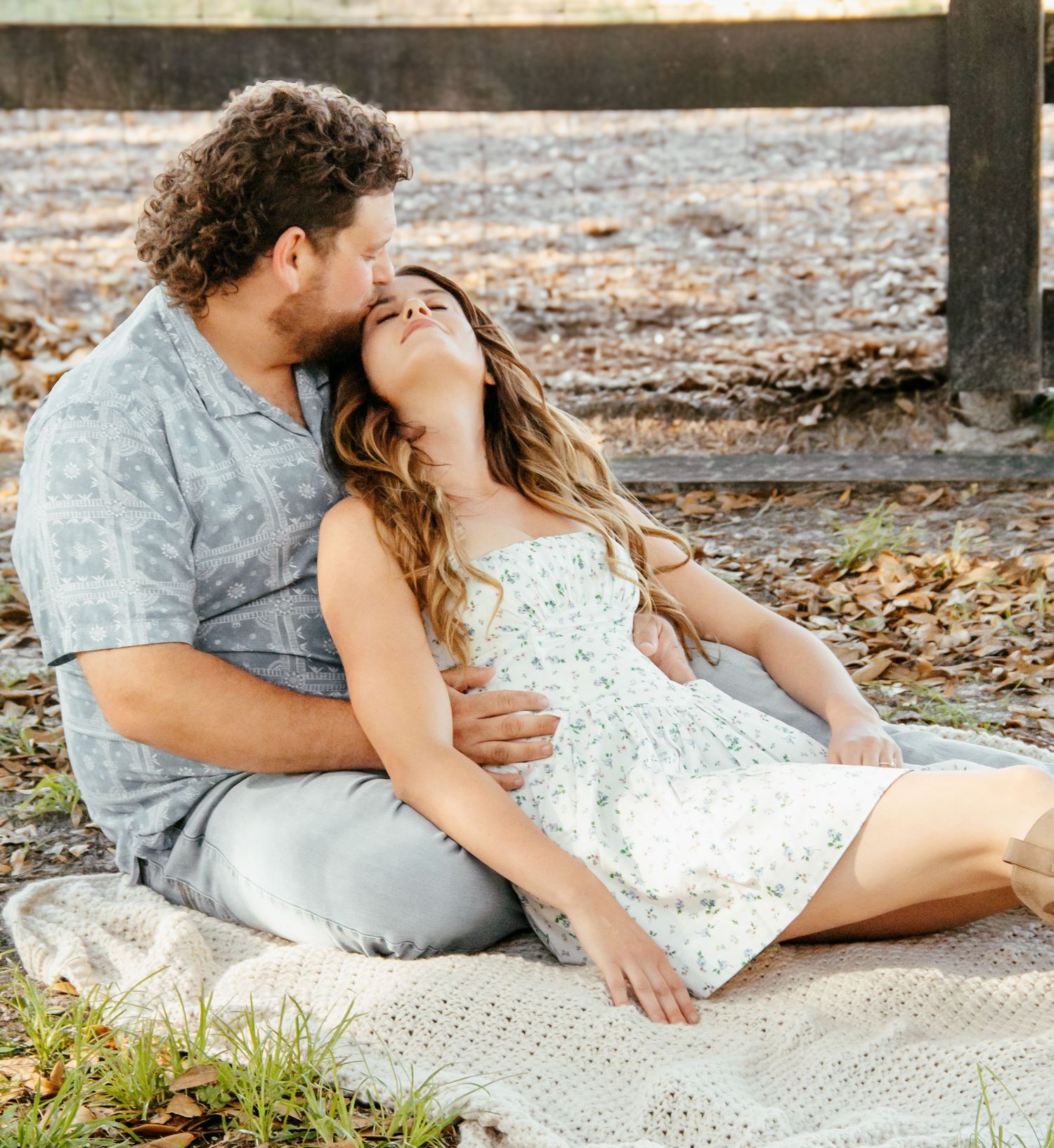 Couple sitting on a blanket outdoors, sharing a romantic moment surrounded by autumn leaves.