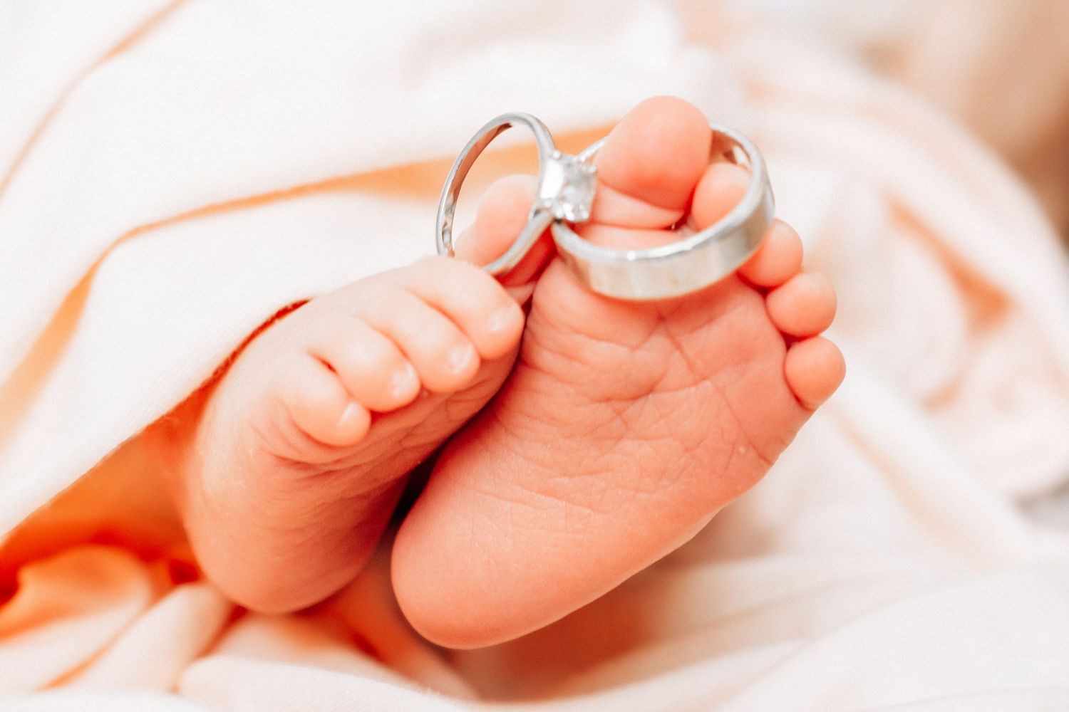 Close-up of newborn baby feet with silver wedding rings, symbolizing new family and marriage.