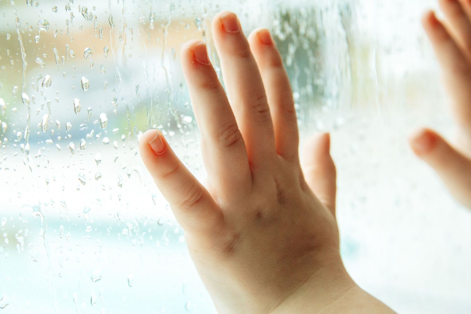 Small hands touching a window with raindrops and condensation.