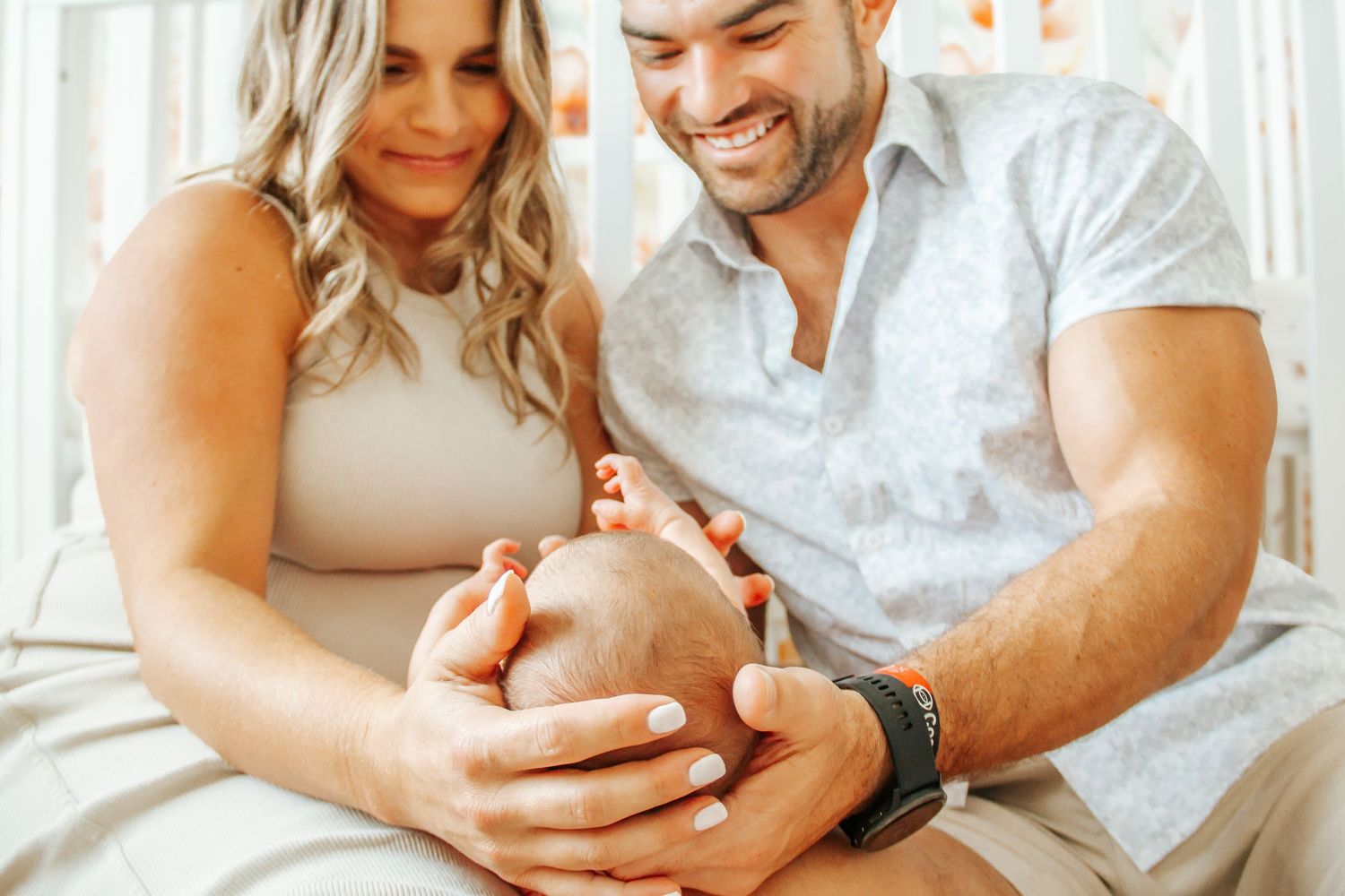 Happy couple smiling and cradling their newborn baby together in a bright, cozy nursery setting.