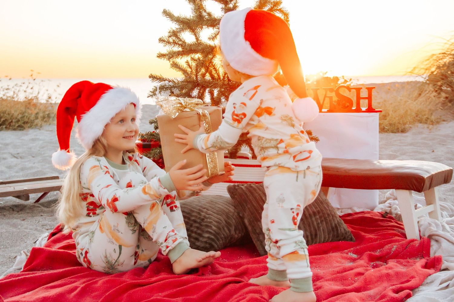 A festive Christmas photo shoot at sunset features red and white decor with a cozy blanket and holiday decorations.