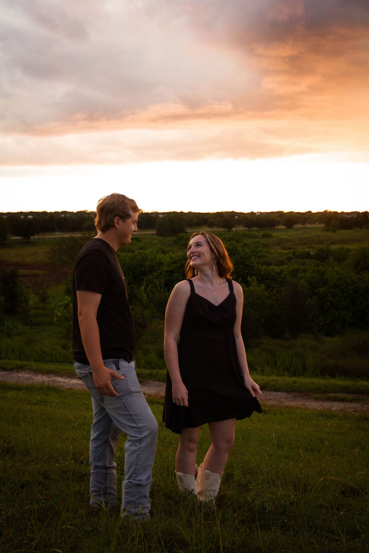 Couple in black outfits sharing a joyful moment at golden hour sunset in a lush green field.