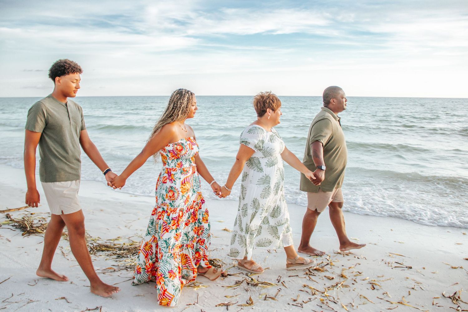 A family walks hand in hand along a serene beach shoreline with gentle waves at sunset.