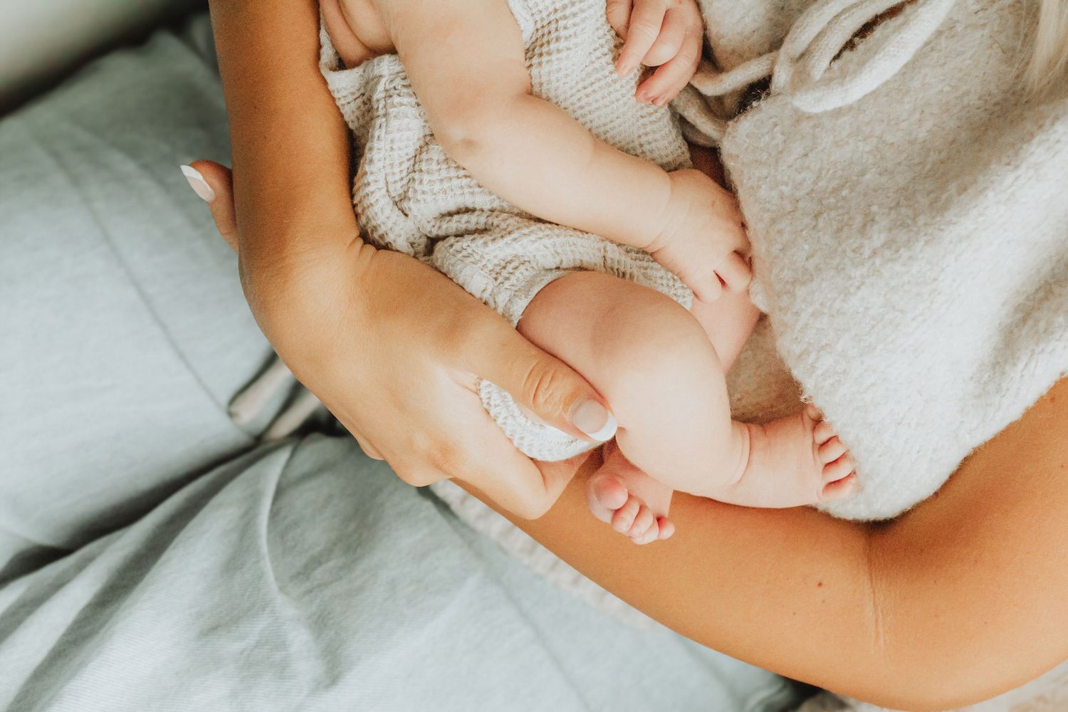 Close-up of a mother cradling her newborn baby's tiny feet and legs in her arms on a soft bed.