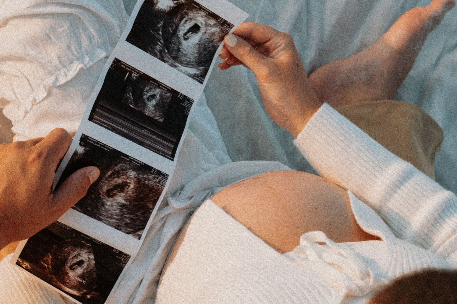 Pregnant woman holding ultrasound sonogram photos while resting, showing baby scans during pregnancy.