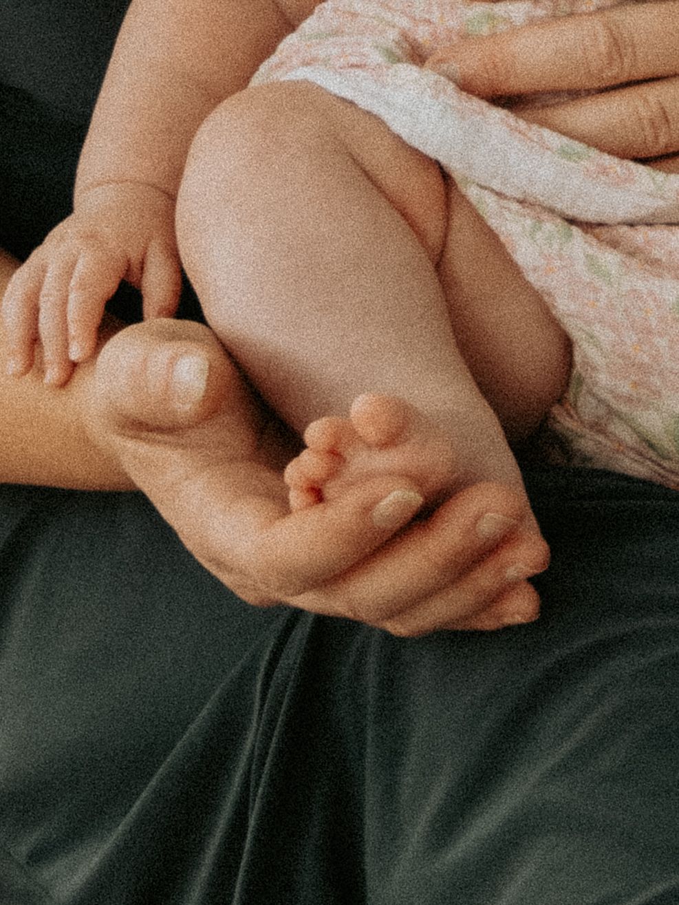 A parent gently cradles a newborn baby's tiny feet and legs in their hands, showing the delicate bond between parent and child.