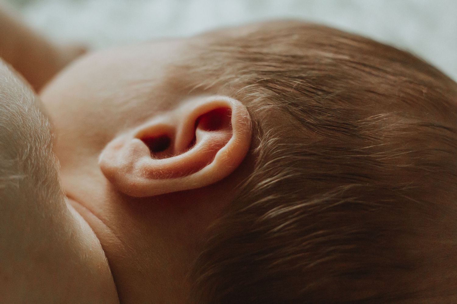 Close-up of a newborn baby's delicate ear with fine hair, showcasing the intricate details of infant anatomy.