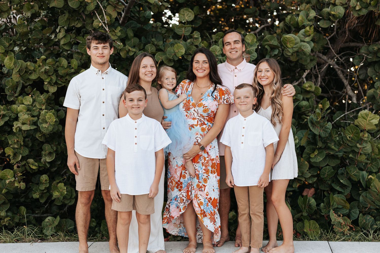 Family group portrait outdoors with everyone coordinated in white and floral outfits.