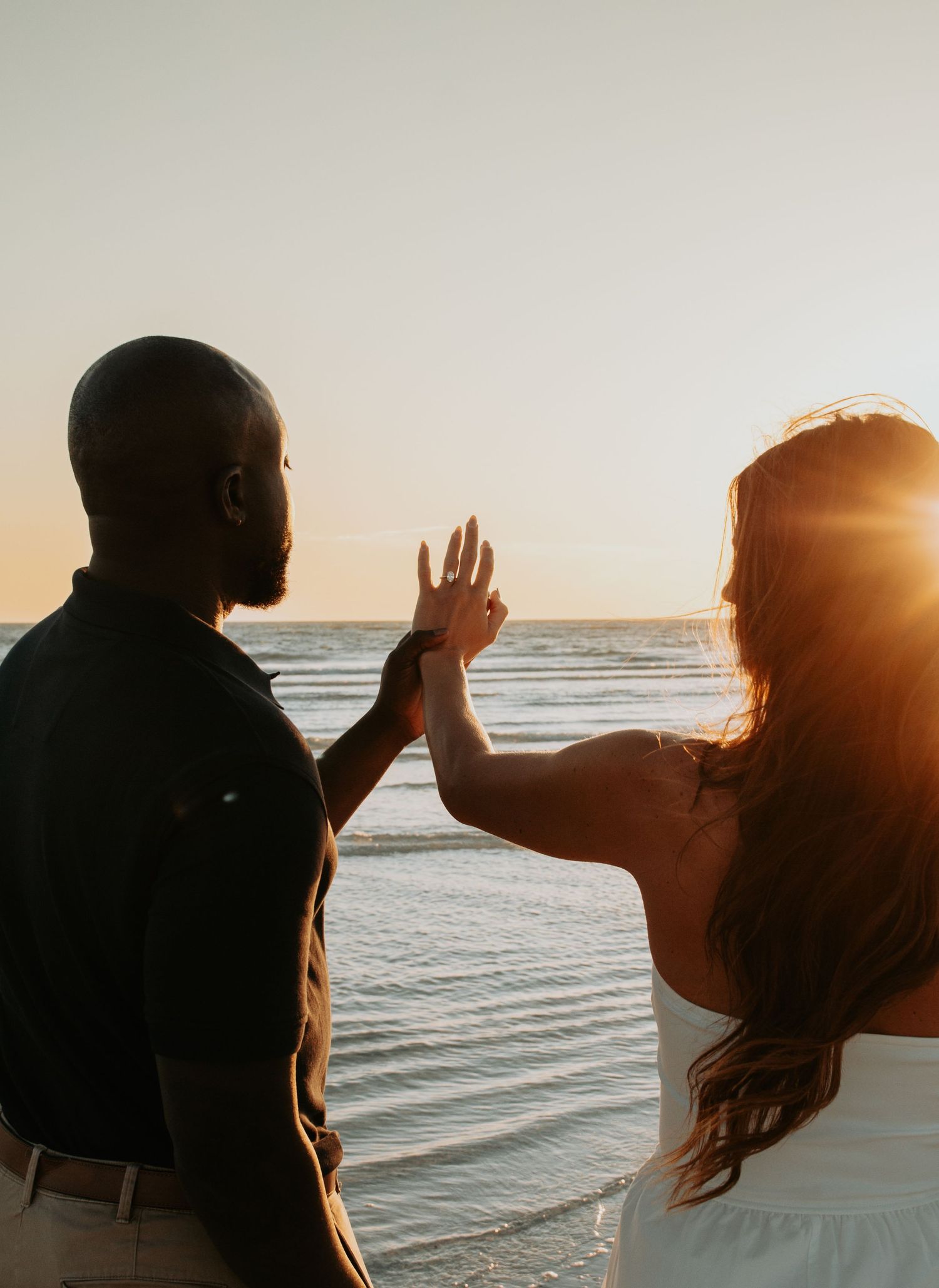 Couple holding hands at sunset on the beach, silhouetted against golden ocean light.