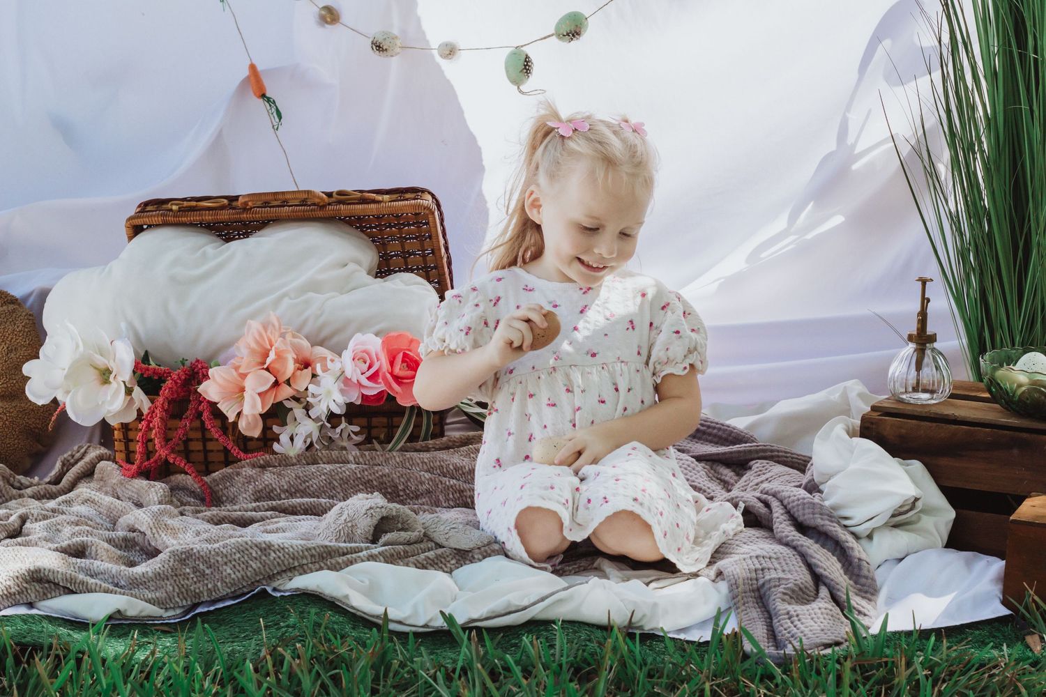 Dreamy scene with small child on white linens surrounded by floral arrangements and hanging decorations.