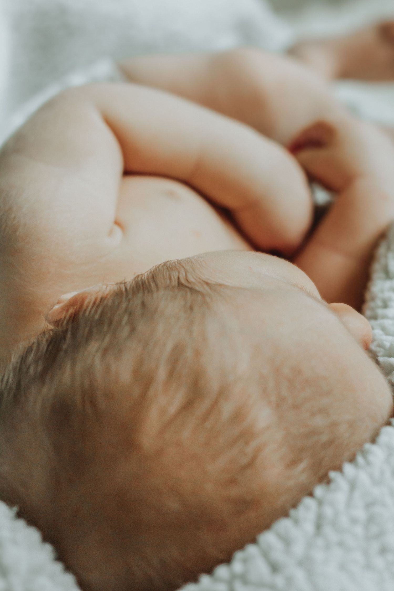 Close-up of a sleeping newborn baby lying on a soft white blanket, showing delicate skin folds and tiny fingers.