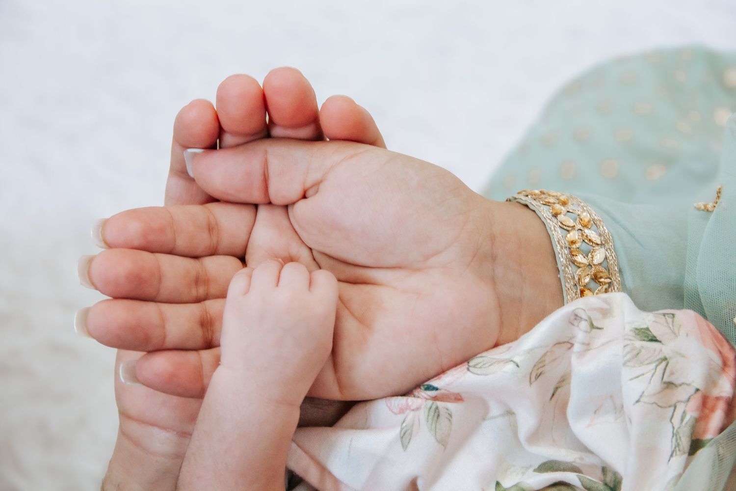 A mother gently holds her newborn baby's tiny feet in her hands, wearing a delicate gold bracelet.