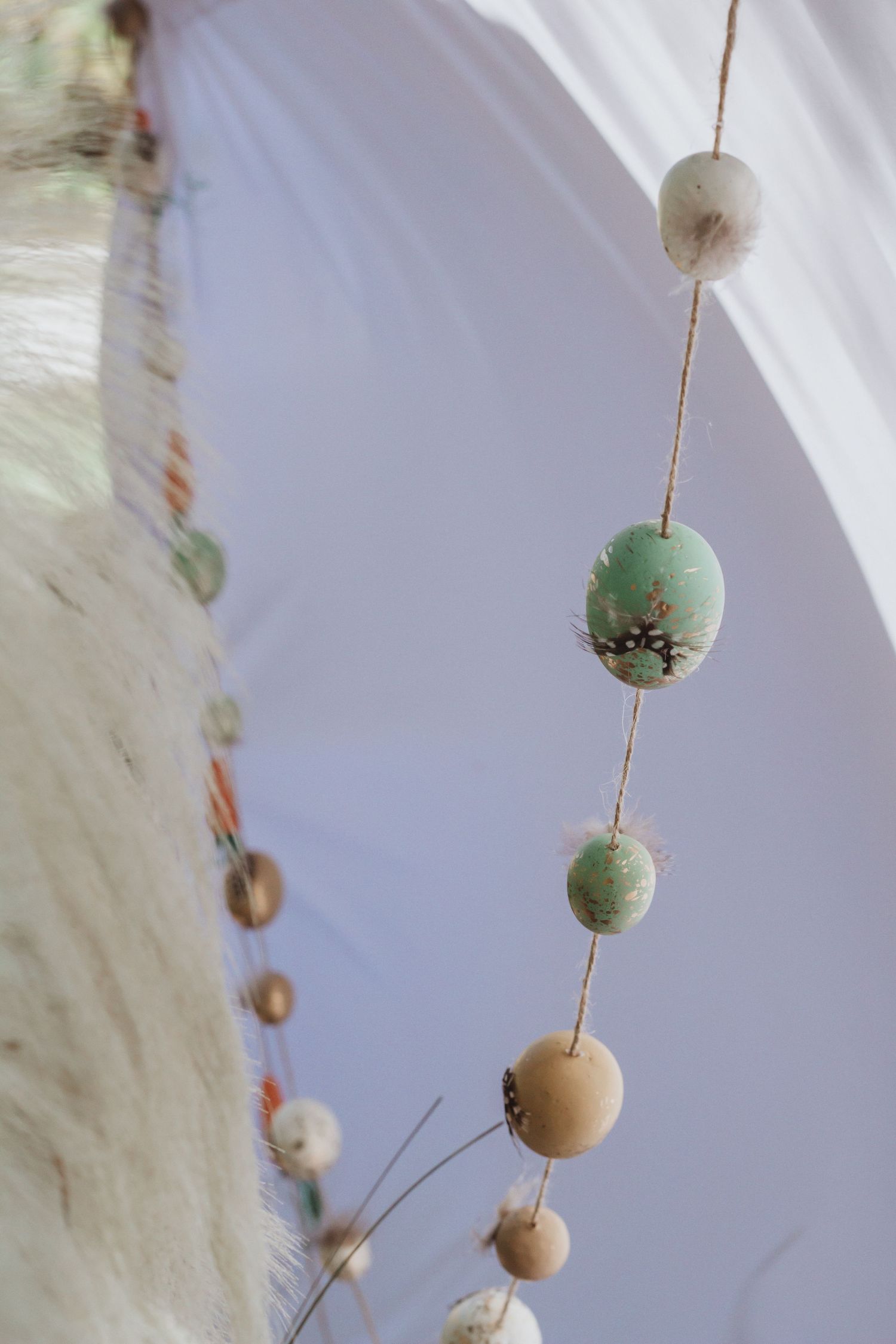 Hanging decorative ornaments in soft green and natural tones against white background.