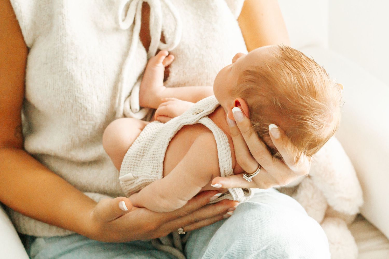 Mother breastfeeding her newborn baby in a cozy, bright room while wearing a casual knit vest.
