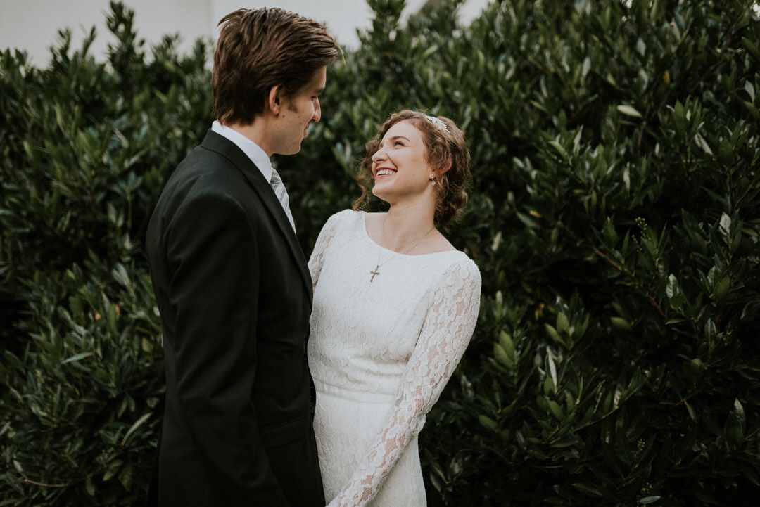 Intimate moment between newlyweds against lush green foliage background.