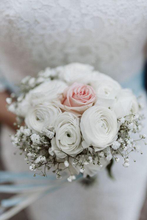 Elegant white and blush pink rose wedding bouquet with baby's breath and ranunculus flowers in soft focus.
