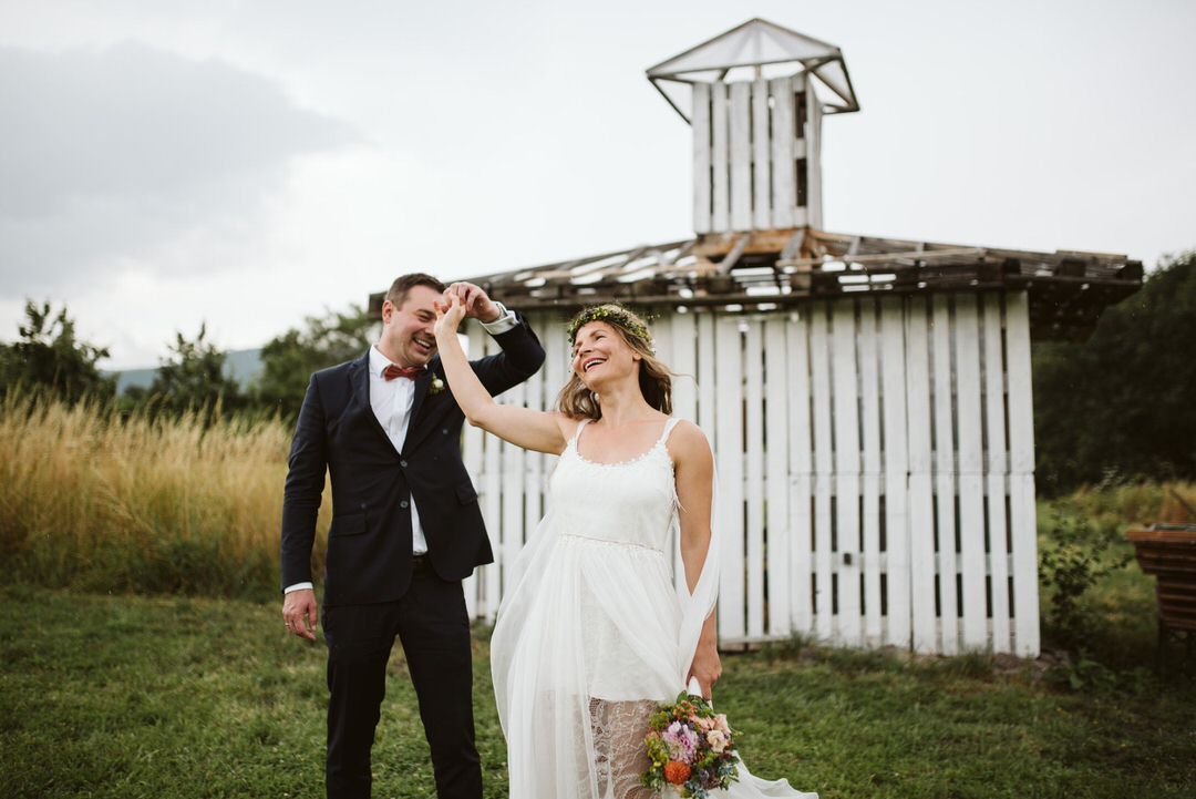 Wedding couple laughing together in front of rustic white chapel building.
